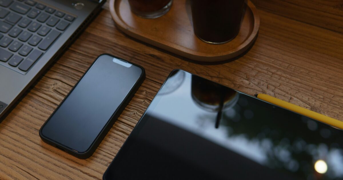 カフェの木製テーブルに置かれたスマホとタブレットとノートパソコン
